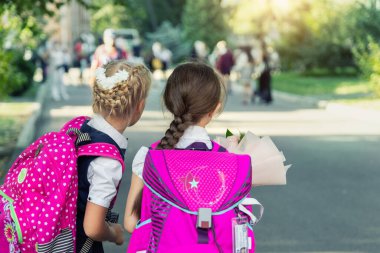 Okula dönen, üniforma giyen ve çiçek buketi takan, büyük pembe sırt çantalı, sevimli, sevimli, küçük beyaz okul kızlarıyla dolu. Birinci sınıf ilköğretim mutlu öğrenciler.