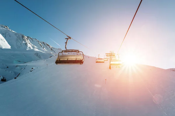 阳光明媚的夜晚 滑雪车在高山山地冬季度假胜地空旷的缆车上 滑雪椅拉索的方式与人们喜欢滑雪和滑雪板 夕阳西下的天空在背景上闪烁着光芒 — 图库照片