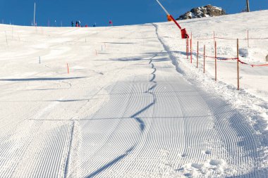 Yakın çekimde, parlak güneş ve açık mavi gökyüzü arkaplanlı yeni hazırlanmış kayak pisti. Avrupa kış kayak merkezindeki karlı dağ manzarası.