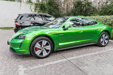Kyiv, Ukrayna - 6 Eylül 2020: Mamba yeşil metalik renkte yeni elektrikli sıfır emisyonlu Porsche Taycan turbo sonbahar günü ormanda şehir caddesine park edildi.