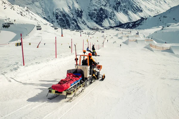 Snowmobile machine with sled and equipment riding fast hurry up driver to help injured skier or snowboarder at accident on winter mountain resort. Emergency rescue vehicle at ski slope piste downhill
