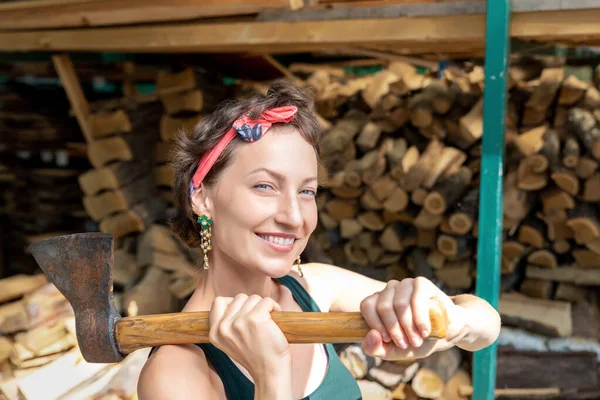 Young adult beautiful happy attractive caucasian brunette woman portrait have fun enjoy holding old rusty axe chopping firewood at wood store on backyard. Female person vintage retro pinup style