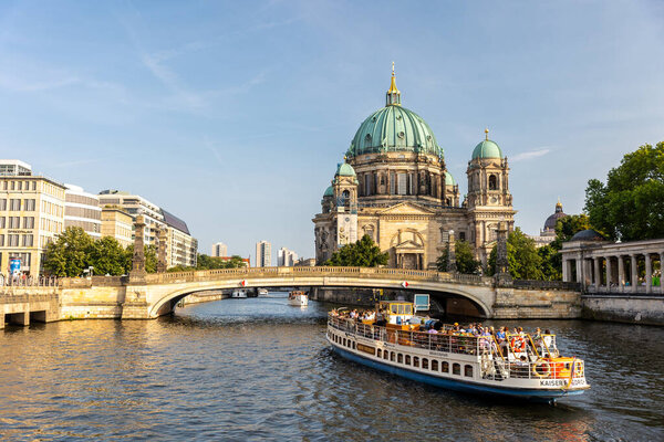Berlin, Germany - August 9th, 2025: Majestic Berliner Dom cathedral rises above river Spree bright sunlight. Sightseeing boat full tourists passes stone bridge, highlighting vibrant city atmosphere.