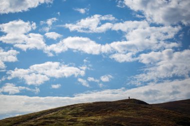 Bir bisikletçi bulutlu bir gökyüzü arka plan üzerinde bir tepenin üstüne küçük bir rakam.