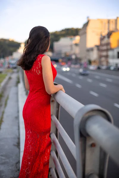 Chica en un vestido rojo está de pie cerca de la valla de la carretera . —  Fotos de Stock