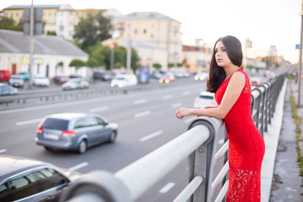 Chica en un vestido rojo está de pie cerca de la valla de la carretera . —  Fotos de Stock
