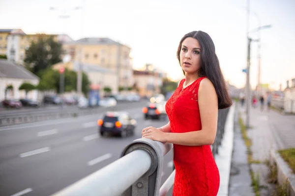 Chica en un vestido rojo está de pie cerca de la valla de la carretera . —  Fotos de Stock