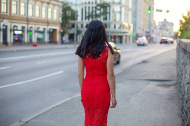 Kırmızı elbiseli bir ince kız kaldırım boyunca yürüyor.