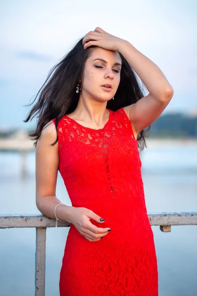 Hermosa joven con un vestido rojo posando en un puente cerca de una vieja cerca . —  Fotos de Stock