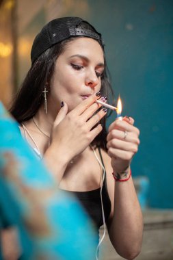 Genç bir kız bir taş merdiven üzerinde otururken ince bir sigara yakıyor. Yakın çekim.