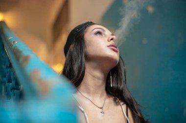 Genç bir kız bir taş merdiven üzerinde otururken ince bir sigara içiyor. Yakın çekim.