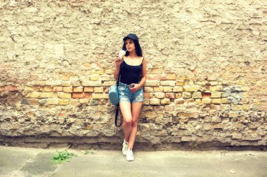 Güzel genç kız içecekler kahve bir tuğla duvar yakınındaki bir saman kağıt bardak.