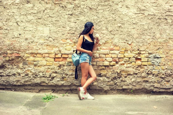 美しい少女は レンガの壁近くストローで紙コップからコーヒーを飲む — ストック写真