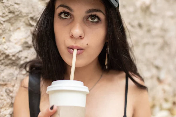 美しい少女は レンガの壁近くストローで紙コップからコーヒーを飲む — ストック写真