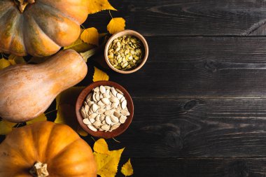 Üç kabak sarı yapraklar siyah bir ahşap zemin üzerinde farklı boyutlarda. Seramik tabak ve ahşap kase kabak çekirdeği ile. Bir tarafta yer. Uzay kopyalayın. Üstten görünüm.