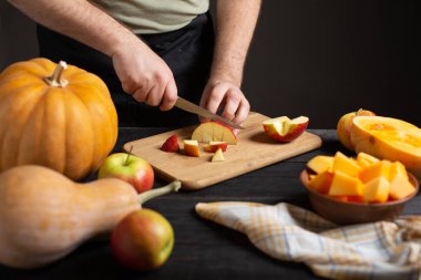 Aşçı pişirme için parçalar halinde elma keser. Ahşap bir siyah masa üzerinde çeşitli boyutları ve şekilleri, Olgun elma, bir bulaşık bezi ve bir kase dilimlenmiş kabak kabak yalan.