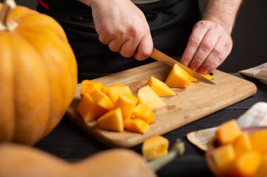 Aşçı pişirme için parçalar halinde kabak keser. Ahşap bir siyah masa üzerinde çeşitli boyutları ve şekilleri, bir bulaşık bezi ve bir kase dilimlenmiş kabak kabak yalan.