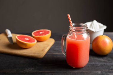 Taze sıkılmış greyfurt suyu bir tanıtıcı bir kavanoza. Siyah ahşap bir masa üzerinde tüm ve dilimlenmiş greyfurt ve beyaz el ile meyve sıkacağı vardır.