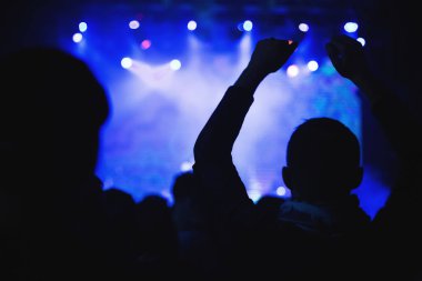 Bir konser kalabalık bir gece kulübünde ışıklı bir sahne önünde siluetleri.