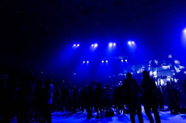 Mavi ışık ışınlarının konser kalabalıkta. İzleyicilerin büyük bir salonda bir rock konserinde siluetleri.