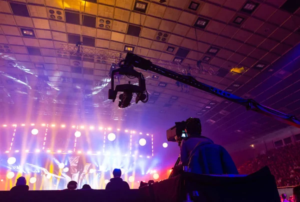 Televizyon bir kameraman tarafından bir konser sırasında. Kamera operatörü ile üzerinde yüksek bir platformdur. Siluetler renkli kiriş arka plan üzerinde.