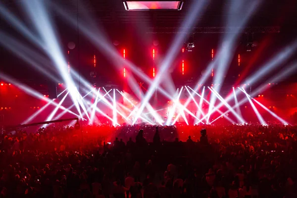 Sahne aydınlatma donanımları güzel ışınları tarafından aydınlatılmış. Eğleniyor büyük salonunda Merkezi'nde konser kalabalık. Televizyon canlı yayın. Birçok kişi doğru sahne bakmak.