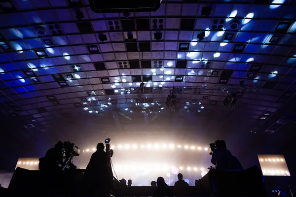 A group of cameramen working during the concert. Television broadcast event. Silhouettes of workers against the background of colorful beams.