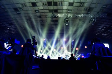 Kameramanlar konser sırasında çalışma grubu. Televizyon yayın olayı. Arka planı renkli kirişler işçilerin siluetleri.