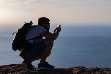 Bir adam bir ada Okyanusu, bir uçurumun kenarında çömelme fotoğraflar. Mirador del Rio, Lanzarote, İspanya.