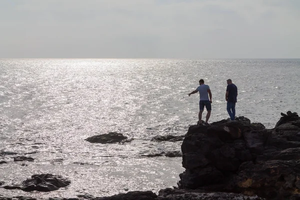 Silhouette of two men standing on a large rock by the ocean. Lanzarote, Spain.