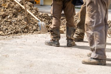 Bir grup işçi kirli giysilerle açık bir çukurun yanında duruyor..