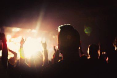 Parlak spot ışığı dans eden insanlar üzerinde parlıyor. Seyirciler müzisyenleri alkışlıyor. Bir konser kalabalığın Silueti.