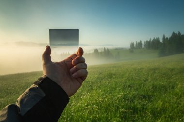 Sisli bir vadinin arka planında bir fotoğrafçının elinde degrade filtre.