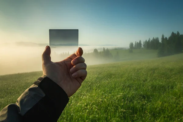 Gradient filter in the hand of a photographer on a background of a valley with fog. — Stock Photo, Image