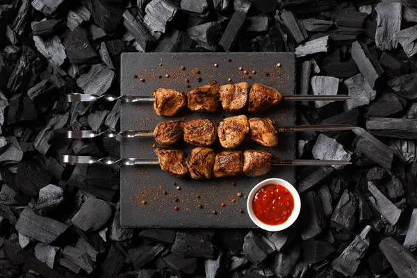 Şiş kebap şiş. Üç porsiyon ızgara et, baharatlı ve soslu. Kömür arka planı. Üst görünüm.