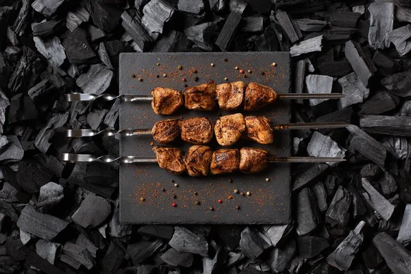 Şişe kebap. Taş bir tabakta üç porsiyon ızgara et. Kömür arka planı. Üst görünüm.