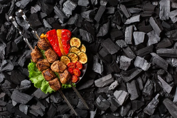 Şişe şiş kebap ve ızgara tatlı biber, kabak, kiraz, yuvarlak tabakta domates. Kömür arkaplanı.