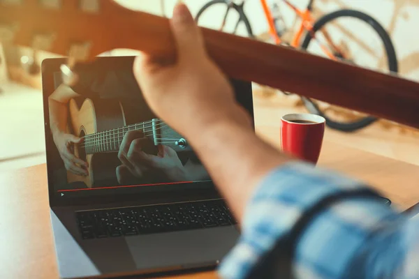 Adam online video dersleri kullanarak gitar çalmayı öğreniyor. Uzaktan iletişim ve eğitim kavramı.