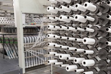 Fabrika ekipmanları perspektifte. Kumaş dokumak için polipropilen ipliklerle dolu sıralar. Otomatik makine. Kimse..