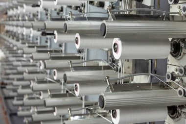 Fabrika ekipmanları perspektifte. Kumaş dokumak için polipropilen ipliklerle dolu sıralar. Otomatik makine. Kimse..