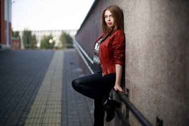 Güzel bir genç kız duvarın arkasında şık kıyafetler içinde kameraya poz veriyor. Mükemmel bir makyaj. Kentsel hipster tarzı.