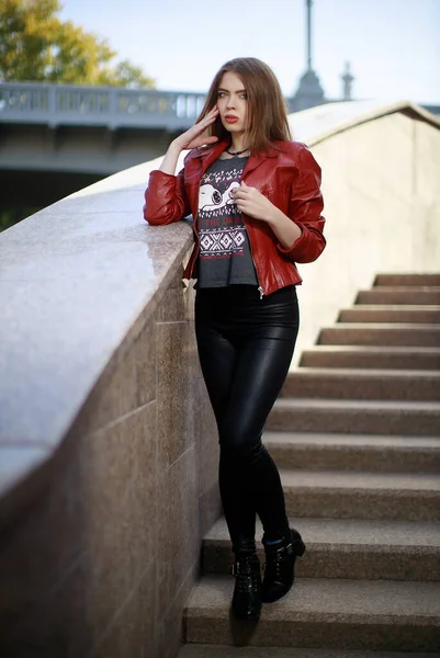 穿着红色皮夹克和黑色腿的年轻漂亮女子的画像留在城市街道的楼梯上 — 图库照片
