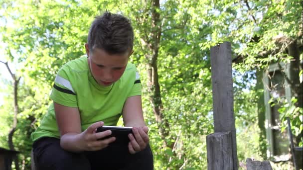 Un niño con una camiseta verde mira en un teléfono inteligente. — Vídeo de stock