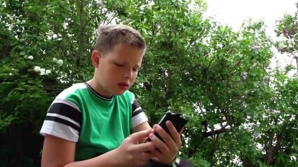 Un niño frustrado utiliza un teléfono inteligente. — Vídeos de Stock