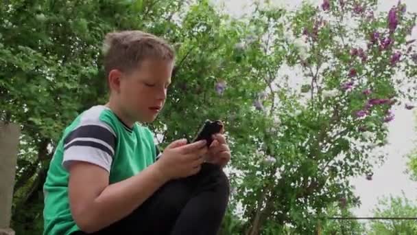 Een jongen in een groen T-shirt gebruikt een smartphone. — Stockvideo