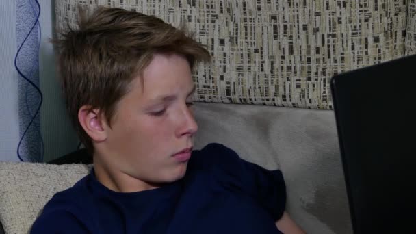 Το αγόρι ξαπλώνει στον καναπέ και παρακολουθεί το λάπτοπ του.. — Αρχείο Βίντεο