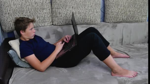 Pojken använder laptopen som ligger i soffan. — Stockvideo