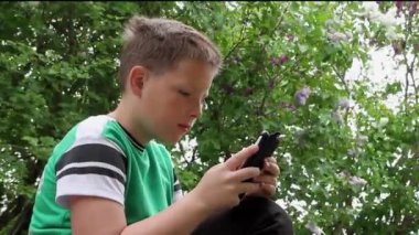  Bir çocuk telefonuyla ağaçların arkasında oynuyor..