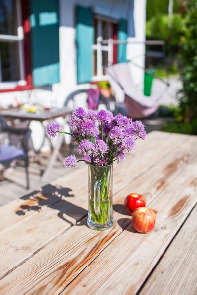 紫色の花が2つのりんごで木製のテーブルの上にガラスのコップに立っている — ストック写真