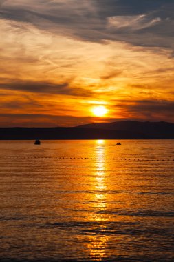 Güneşile denizde turuncu gün batımı, dağların arka planda güzel bir gökyüzü